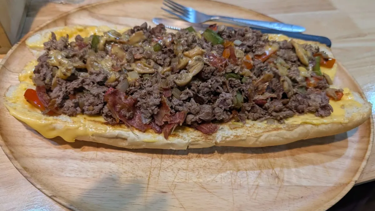 The Super 12" Ultimate at Mano's Cheesesteaks & Burgers in Pattaya - shaved beef, smokey bacon, mushrooms, bell peppers and onions topped with melted cheese on a 12-inch hoagie, served open-face on a wood platter